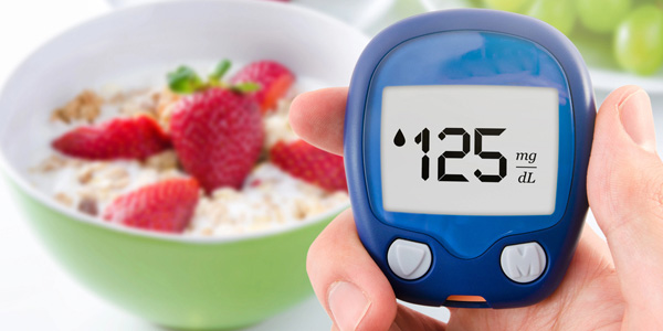 Hand hält ein blaues Blutzuckermessgerät mit Anzeige „125 mg/dL“ vor eine Schale mit Joghurt und Erdbeeren im Hintergrund.